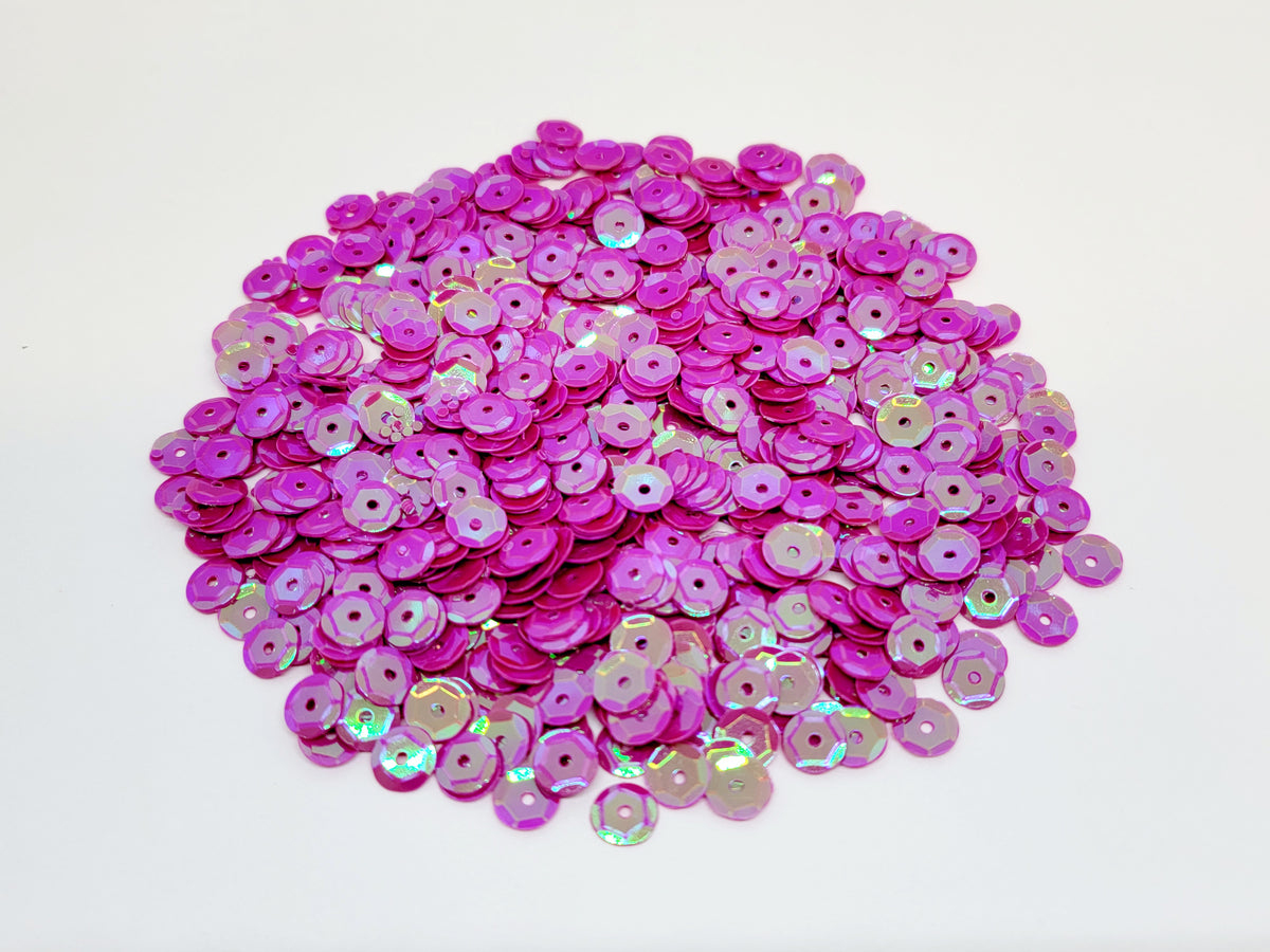 Pile of 6mm round fuchsia sequins with centre holes, on a white background