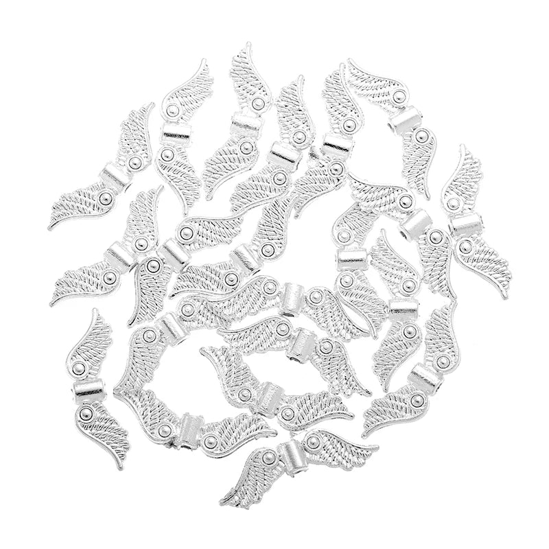 Pile of silver 7 x 24mm angel wing spacer beads on a white background