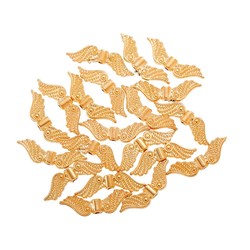 Pile of KC gold 7 x 24mm angel wing spacer beads on a white background