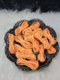 Bundles of 2.7mm apricot suede leather lacing coiled on a dark scalloped dish
