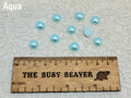 Ten 10mm aqua pearl-look resin half round cabochons (cabs) beside a ruler