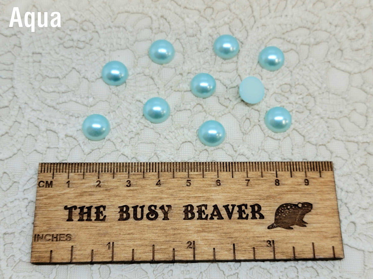 Ten 10mm aqua pearl-look resin half round cabochons (cabs) beside a ruler