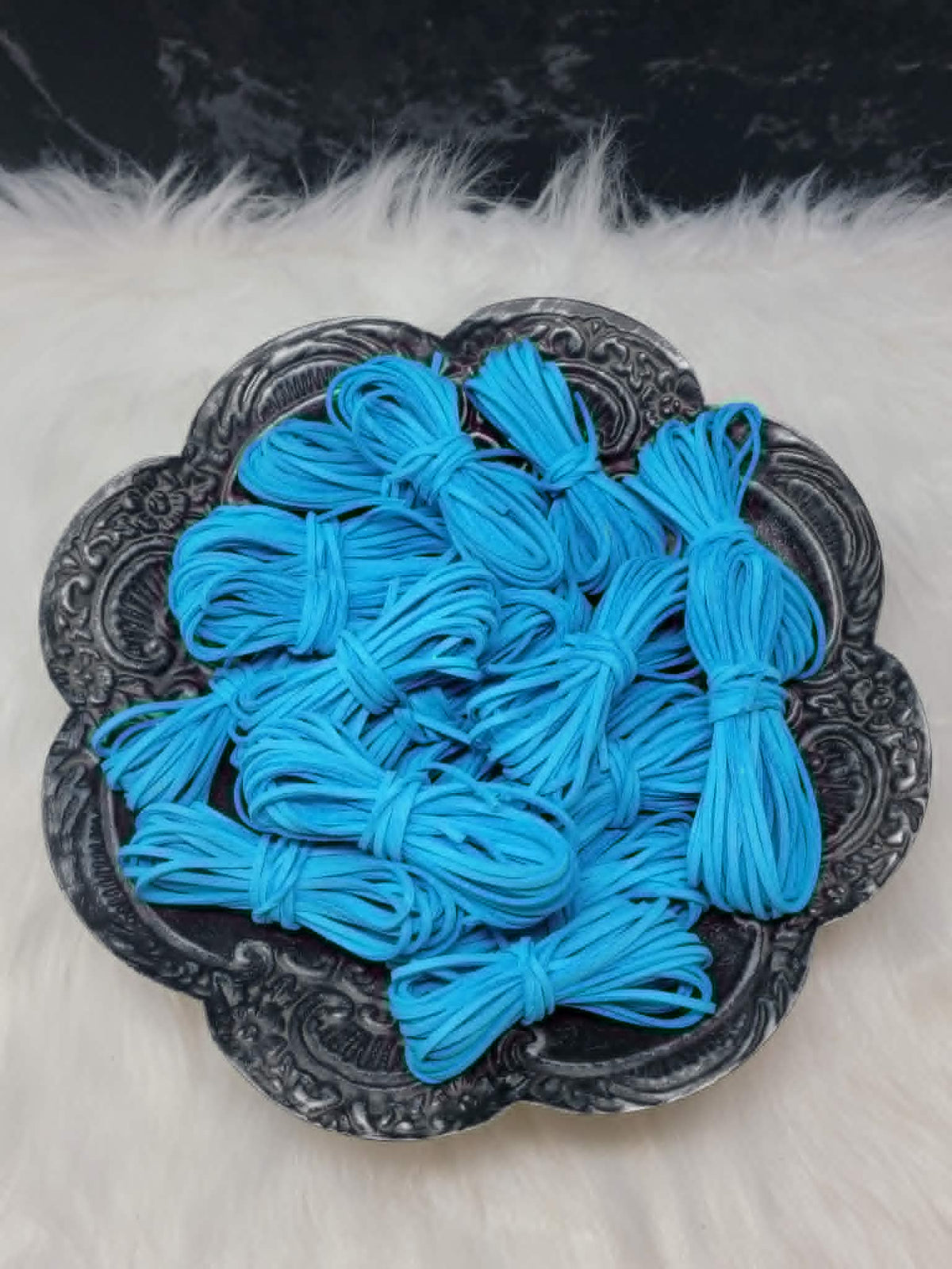 Bundles of 2.7mm aqua suede leather lacing coiled on a dark scalloped dish