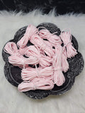 Bundles of 2.7mm baby pink suede leather lacing coiled on a dark scalloped dish