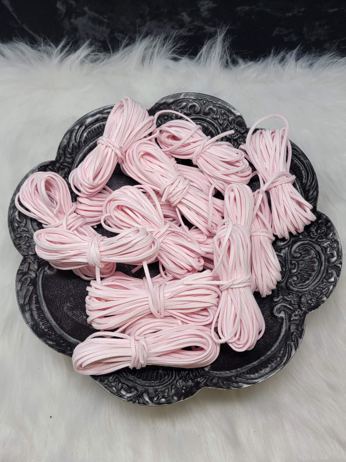 Bundles of 2.7mm baby pink suede leather lacing coiled on a dark scalloped dish