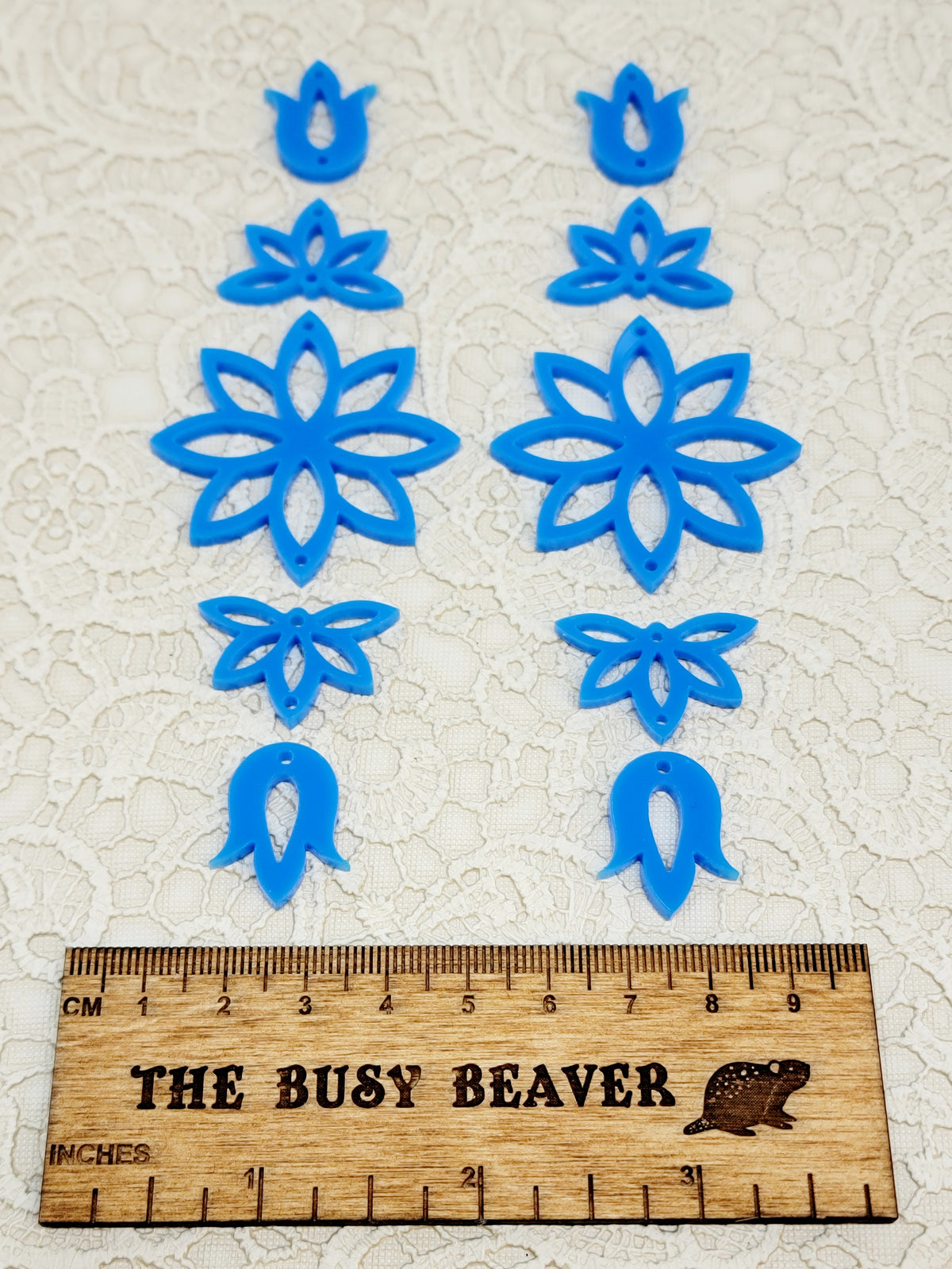 Two 5-tier acrylic flower earring sets in blue, laid out top to bottom beside a ruler