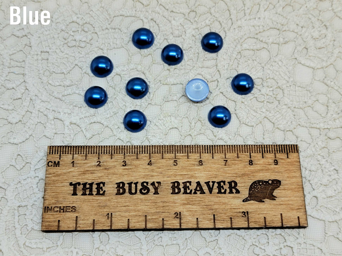 Ten 10mm blue pearl-look resin half round cabochons (cabs) beside a ruler