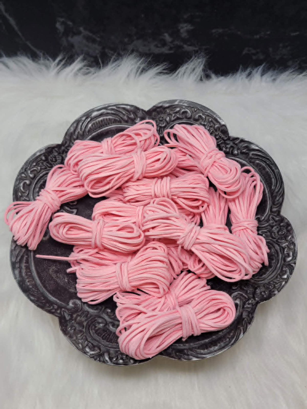 Bundles of 2.7mm bubble gum suede leather lacing coiled on a dark scalloped dish