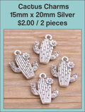 Silver-tone cactus charms with textured detail on a wood background
