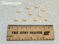 Ten 10mm champagne pearl-look resin half round cabochons (cabs) beside a ruler
