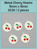 White enamel 16mm heart charms with a red cherry design on a labelled product card