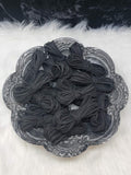 Bundles of 2.7mm black suede leather lacing coiled on a dark scalloped dish