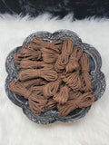 Bundles of 2.7mm coffee suede leather lacing coiled on a dark scalloped dish