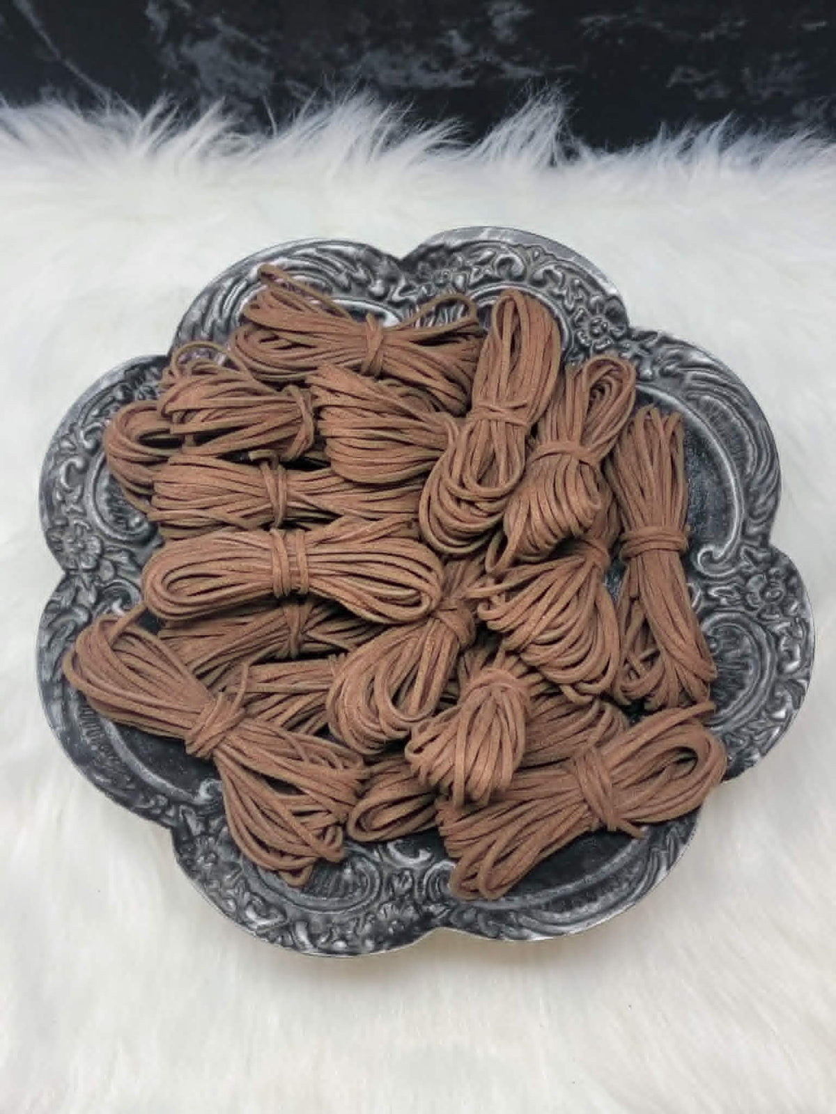 Bundles of 2.7mm coffee suede leather lacing coiled on a dark scalloped dish