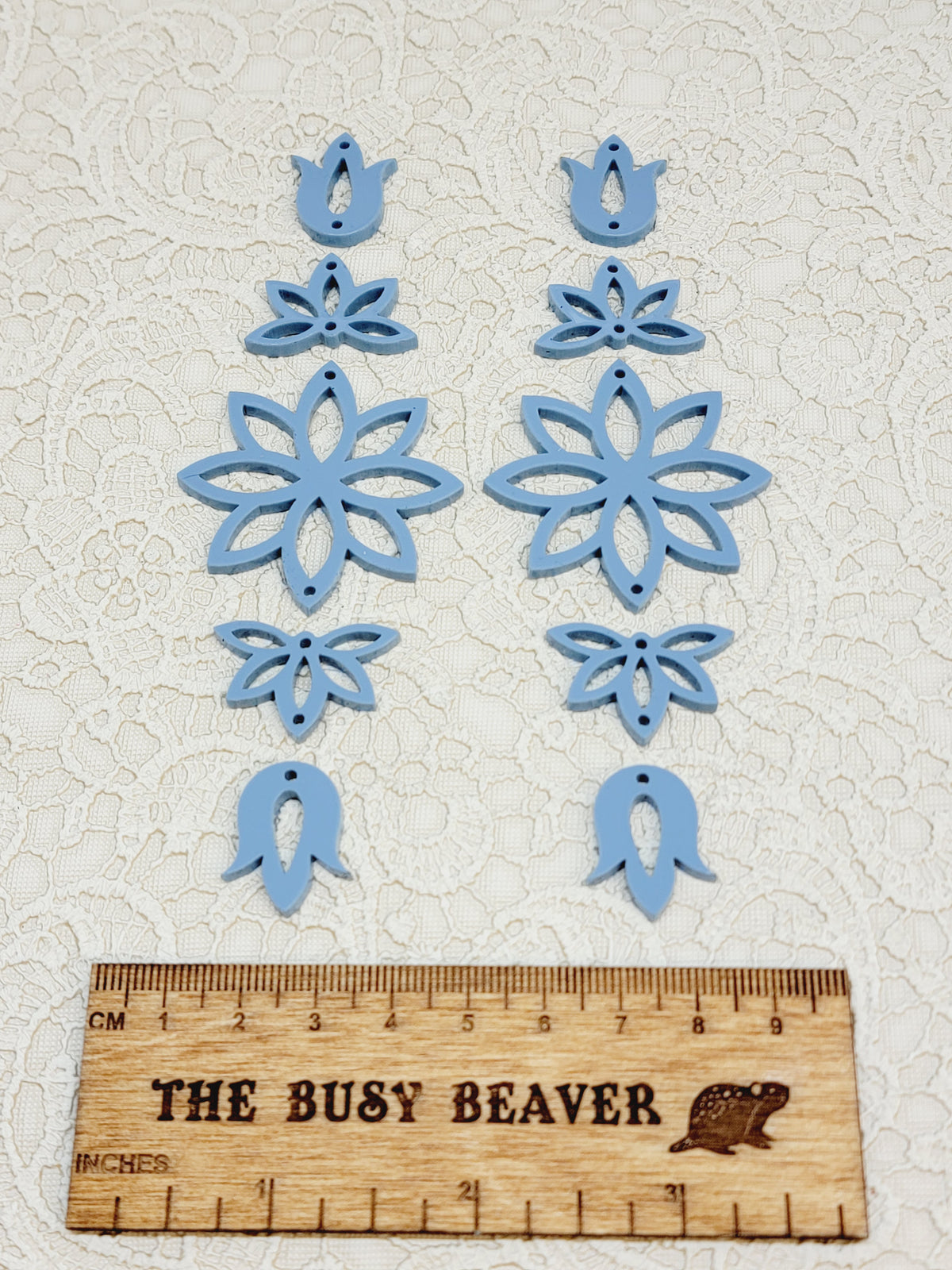 Two 5-tier acrylic flower earring sets in dusty blue, laid out top to bottom beside a ruler
