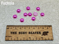 Ten 10mm fuchsia pearl-look resin half round cabochons (cabs) beside a ruler