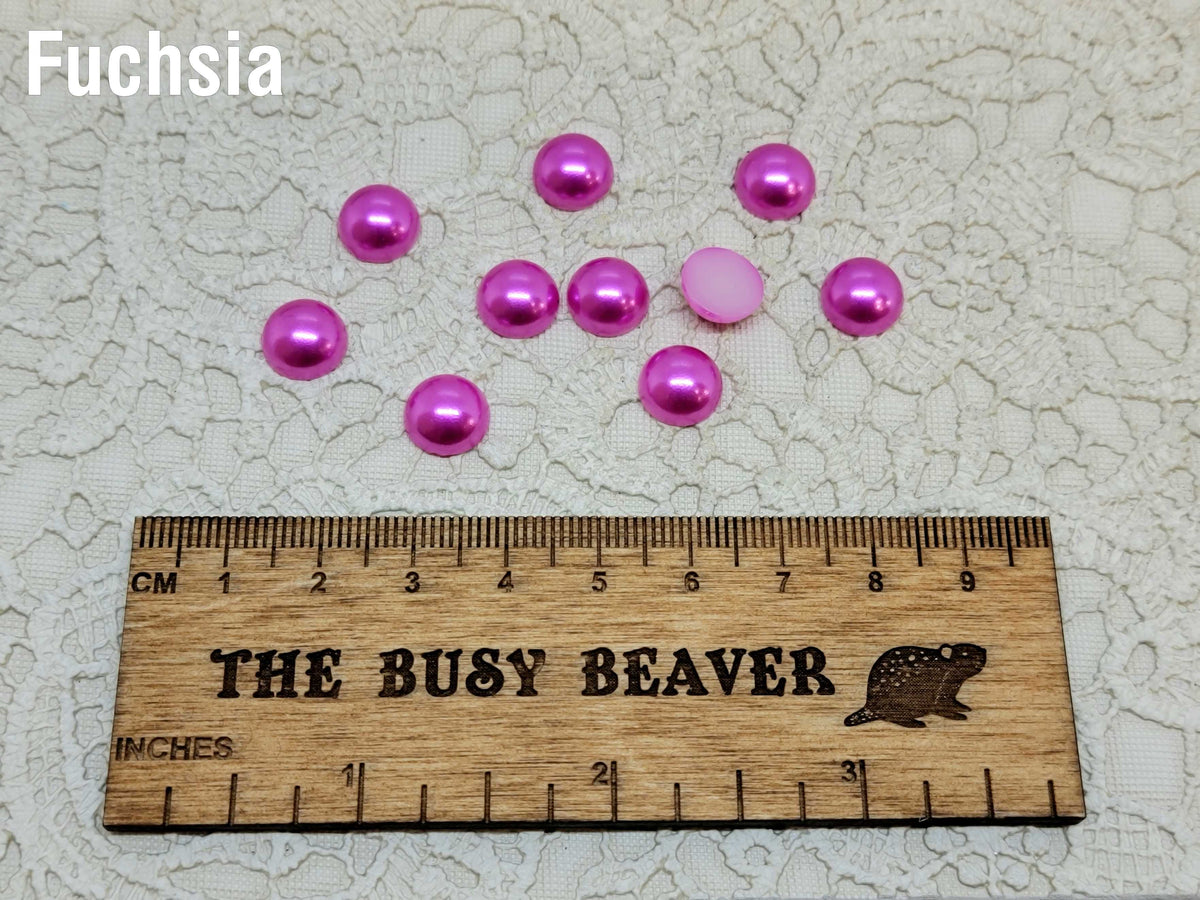 Ten 10mm fuchsia pearl-look resin half round cabochons (cabs) beside a ruler