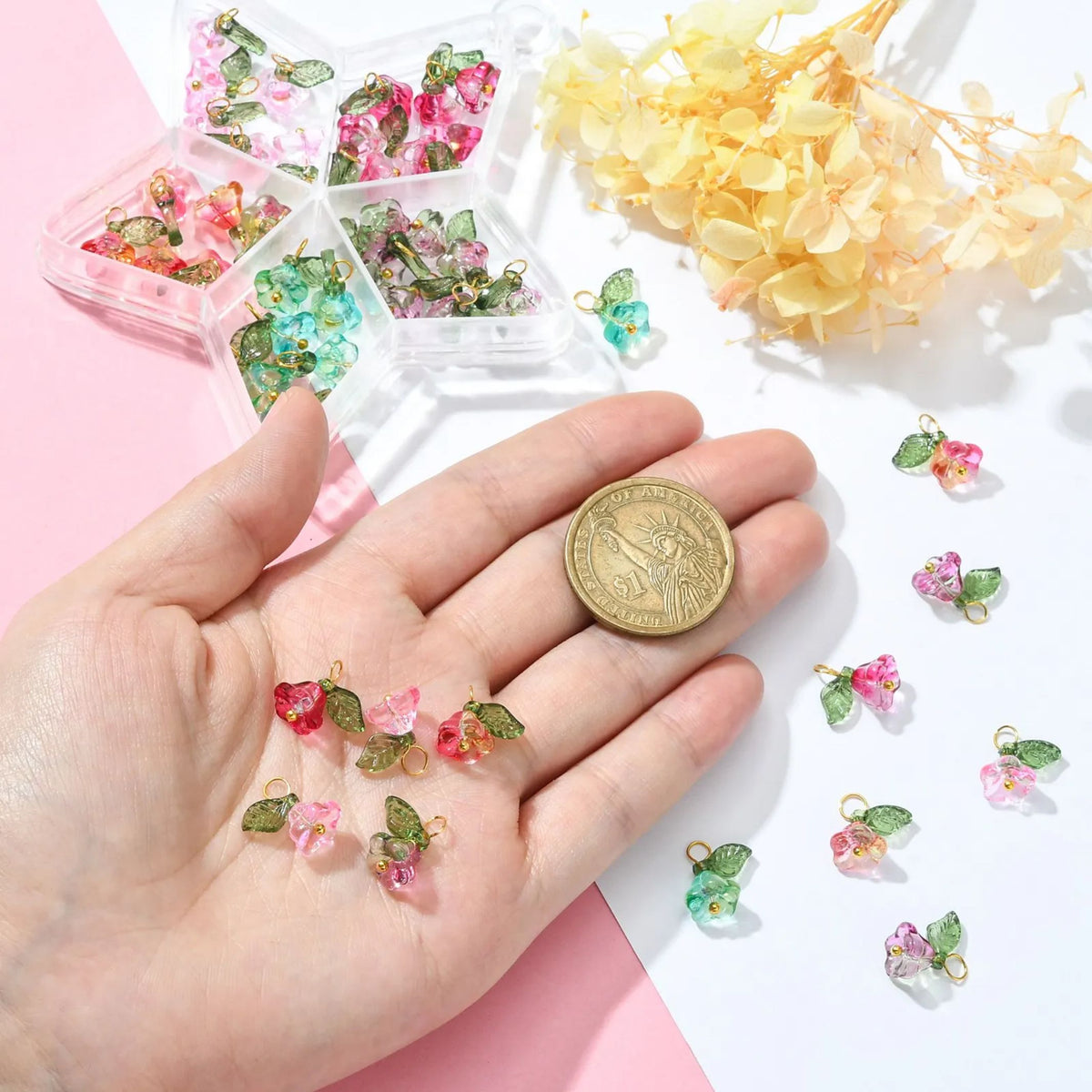 Glass flower and leaf charms held in a palm beside a coin for scale, with the storage case