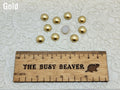 Ten 10mm gold pearl-look resin half round cabochons (cabs) beside a ruler