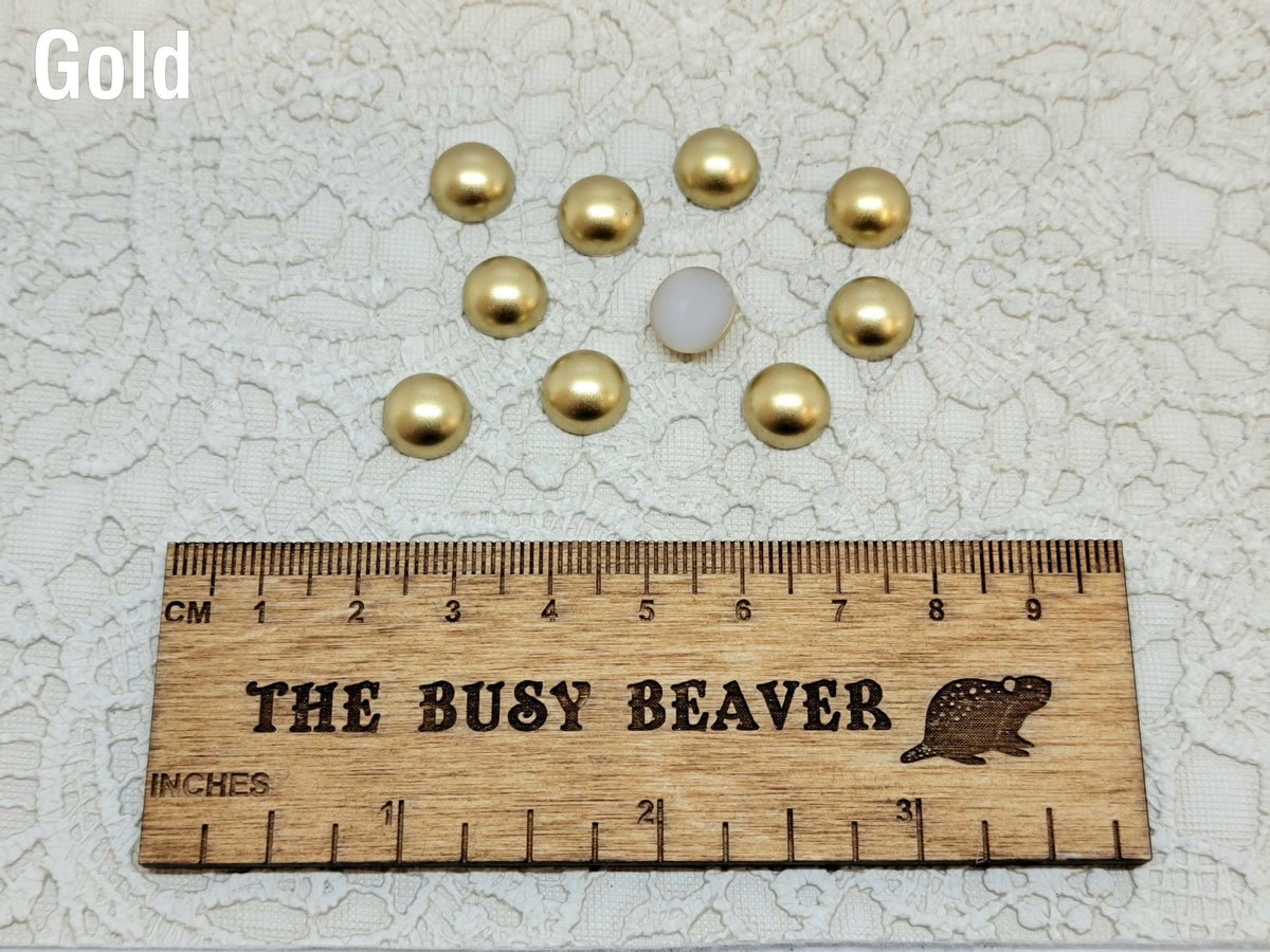 Ten 10mm gold pearl-look resin half round cabochons (cabs) beside a ruler