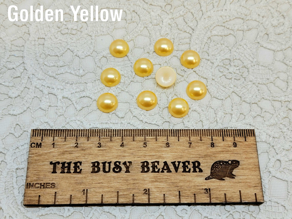 Ten 10mm golden yellow pearl-look resin half round cabochons (cabs) beside a ruler