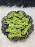 Bundles of 2.7mm grass green suede leather lacing coiled on a dark scalloped dish