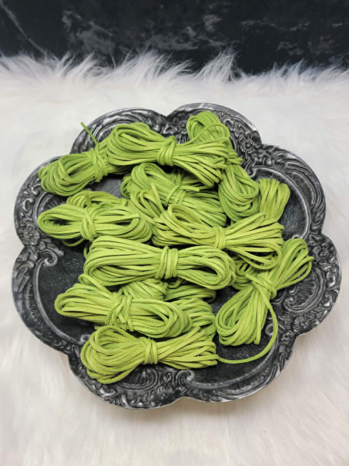 Bundles of 2.7mm grass green suede leather lacing coiled on a dark scalloped dish