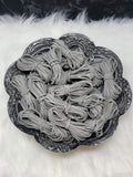 Bundles of 2.7mm grey suede leather lacing coiled on a dark scalloped dish