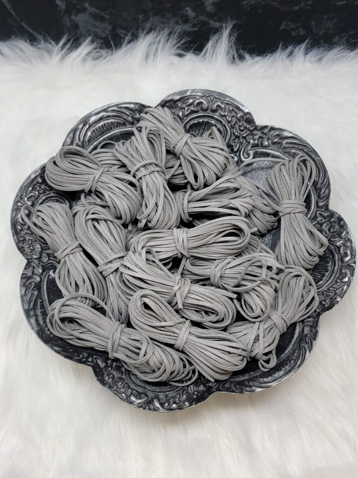 Bundles of 2.7mm grey suede leather lacing coiled on a dark scalloped dish