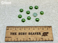 Ten 10mm green pearl-look resin half round cabochons (cabs) beside a ruler