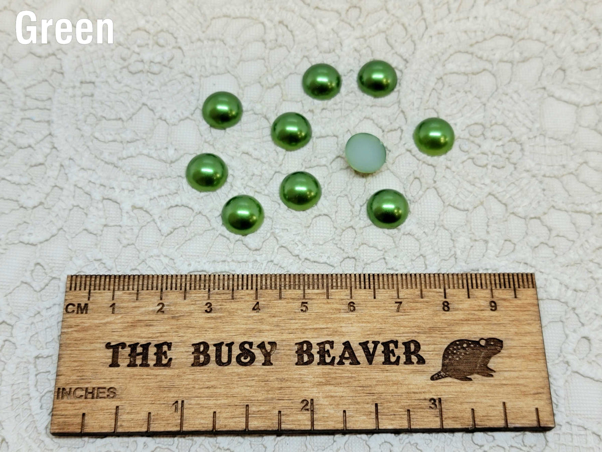 Ten 10mm green pearl-look resin half round cabochons (cabs) beside a ruler