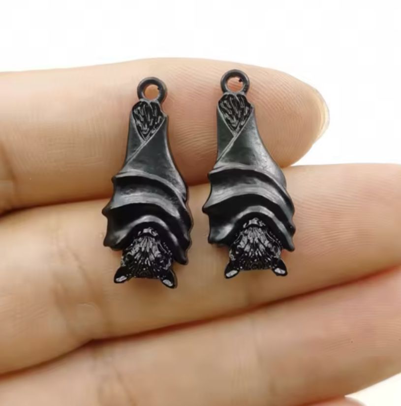 Two dark grey 11 x 27mm hanging bat charms with folded wings, held on a fingertip