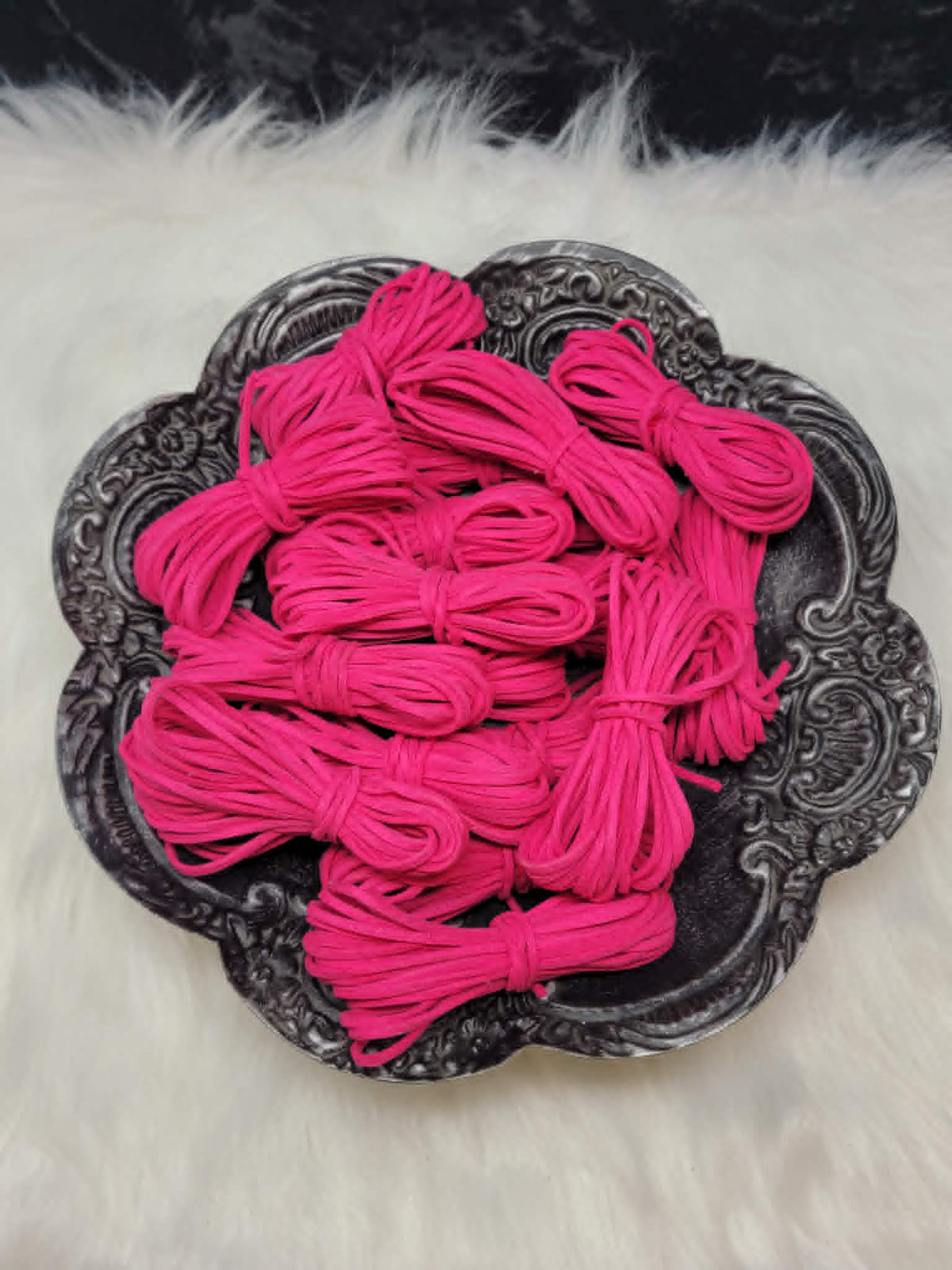 Bundles of 2.7mm hot pink suede leather lacing coiled on a dark scalloped dish