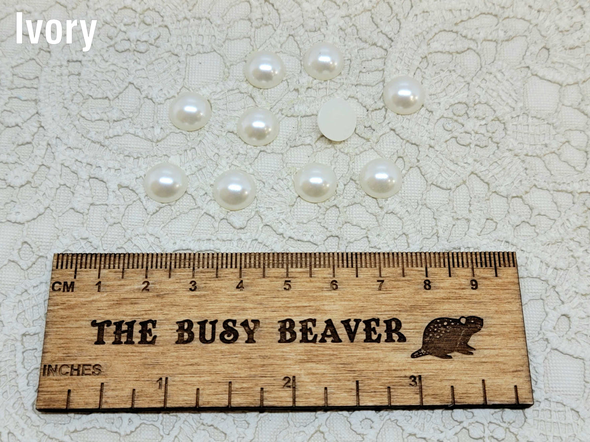 Ten 10mm ivory pearl-look resin half round cabochons (cabs) beside a ruler