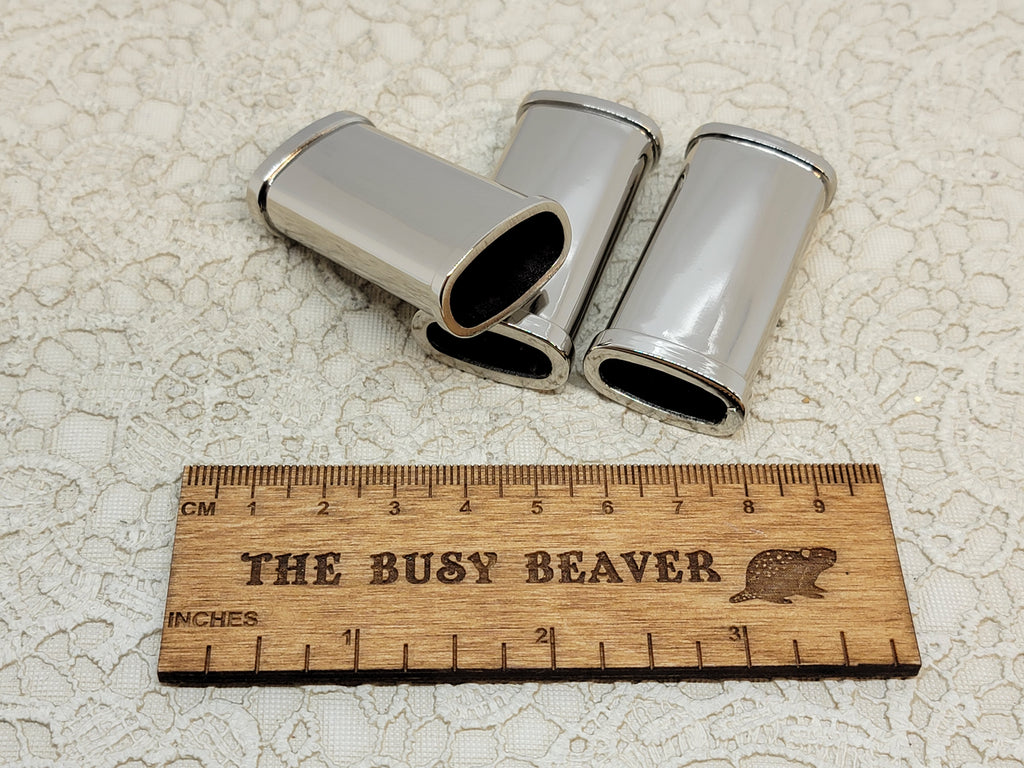 Three blank silver J5 lighter cases with ridged edges beside a ruler