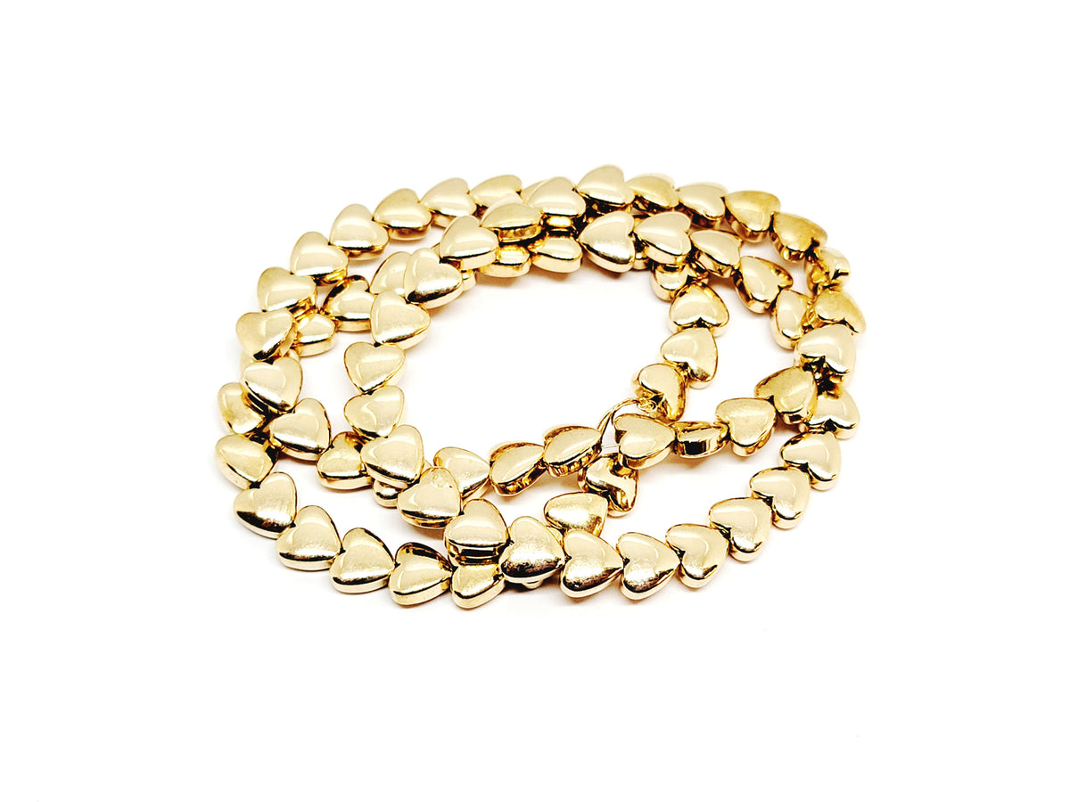 Strand of 6mm KC gold hematite heart beads coiled on a white background