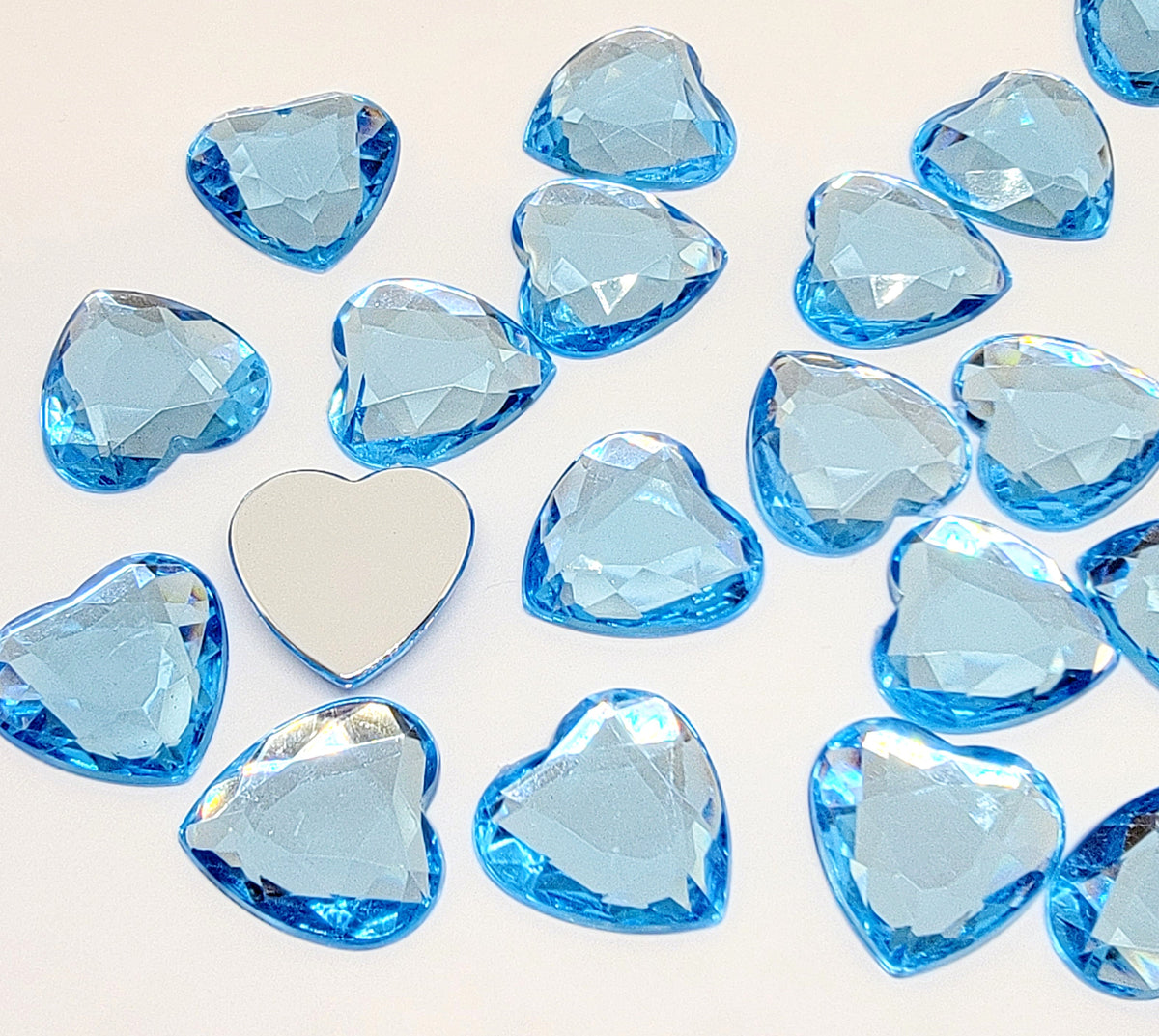 Pile of 20mm faceted light blue resin heart gem cabochons (cabs), one flipped to show the flat back