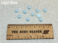 Ten 10mm light blue pearl-look resin half round cabochons (cabs) beside a ruler