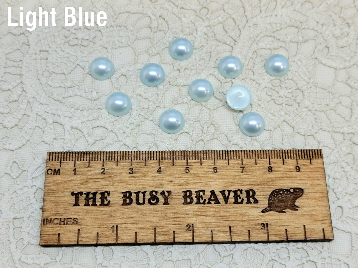 Ten 10mm light blue pearl-look resin half round cabochons (cabs) beside a ruler