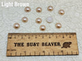 Ten 10mm light brown pearl-look resin half round cabochons (cabs) beside a ruler