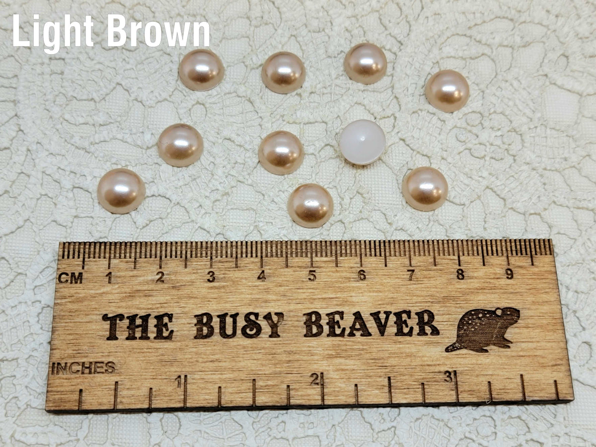 Ten 10mm light brown pearl-look resin half round cabochons (cabs) beside a ruler