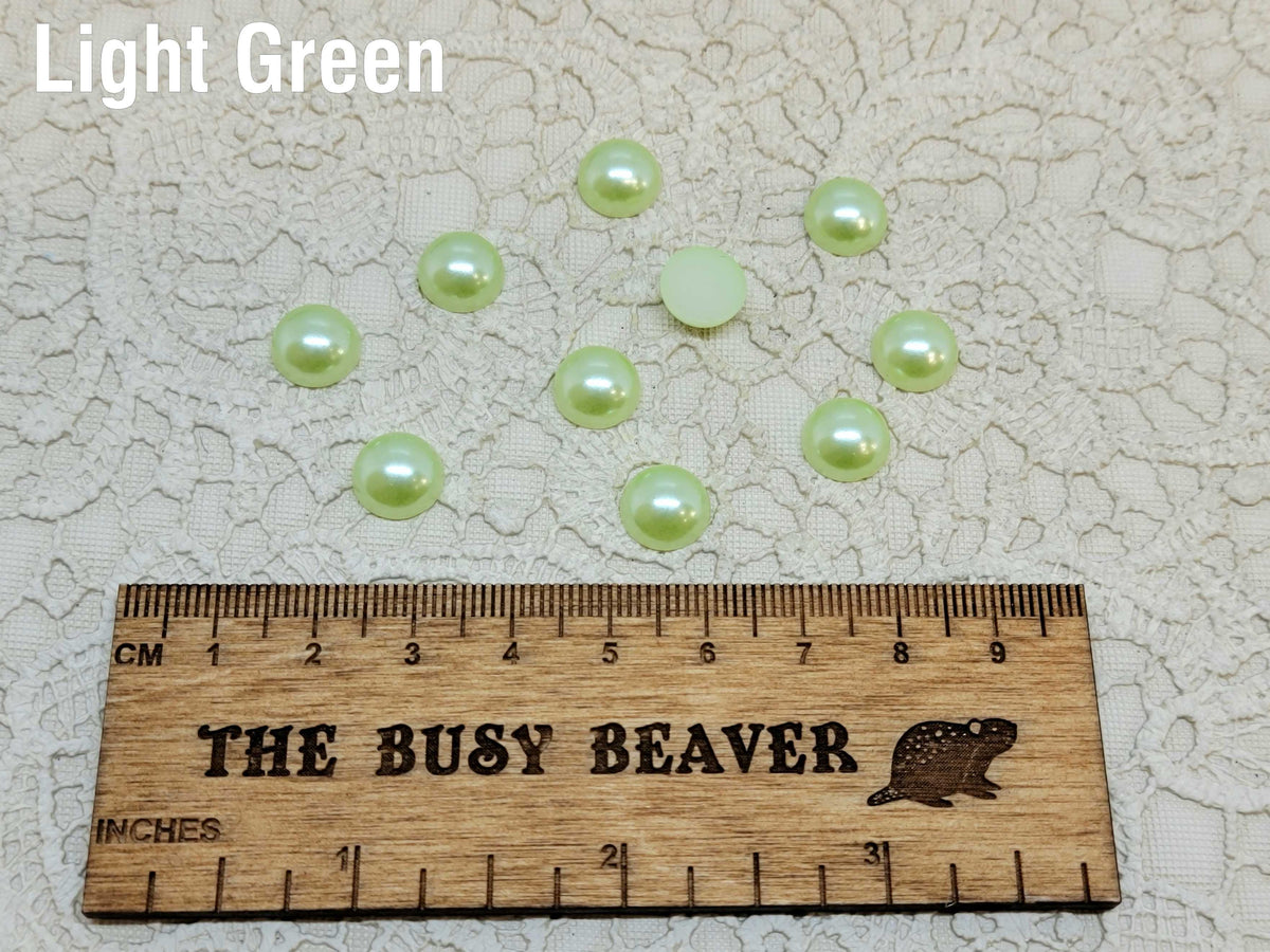 Ten 10mm light green pearl-look resin half round cabochons (cabs) beside a ruler