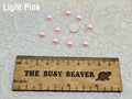 Ten 10mm light pink pearl-look resin half round cabochons (cabs) beside a ruler