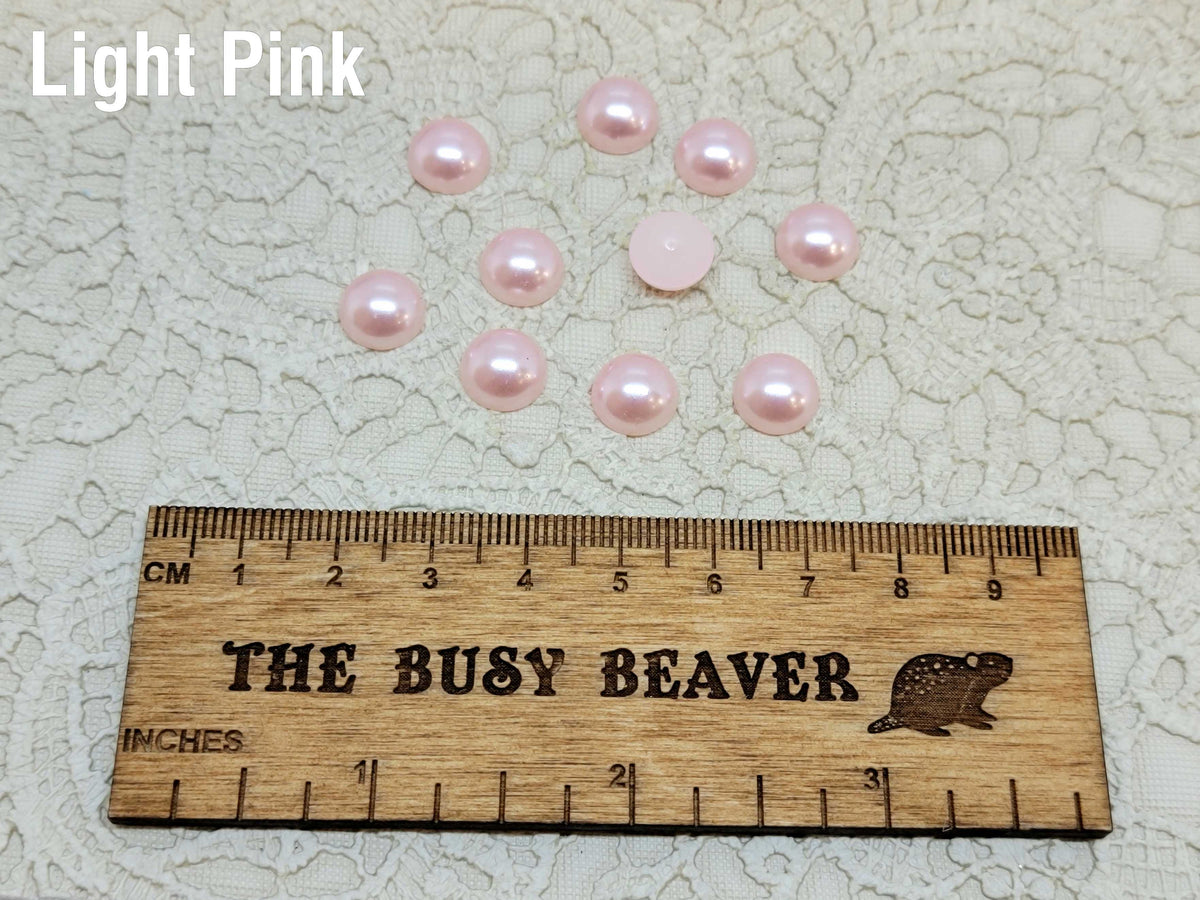 Ten 10mm light pink pearl-look resin half round cabochons (cabs) beside a ruler