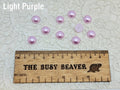 Ten 10mm light purple pearl-look resin half round cabochons (cabs) beside a ruler