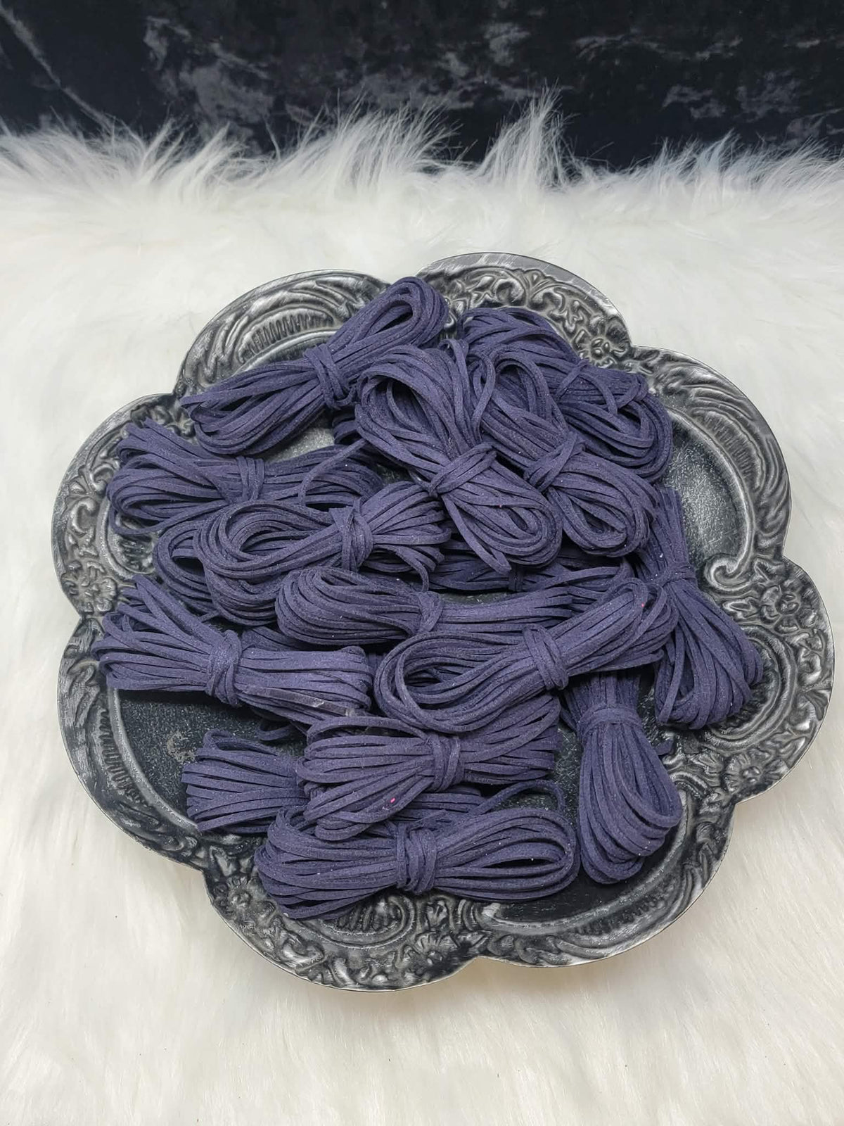 Bundles of 2.7mm midnight blue suede leather lacing coiled on a dark scalloped dish