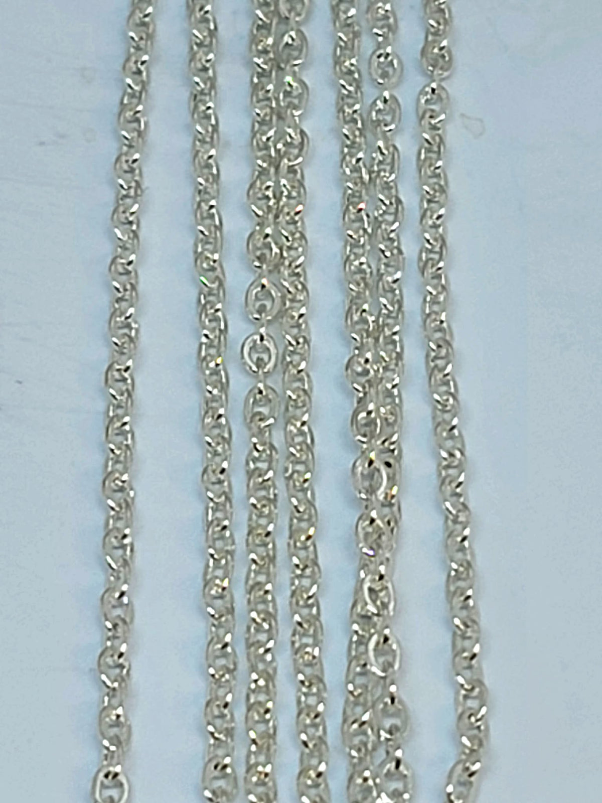 Hanging strands of 2mm silver stainless steel link chain against a white background