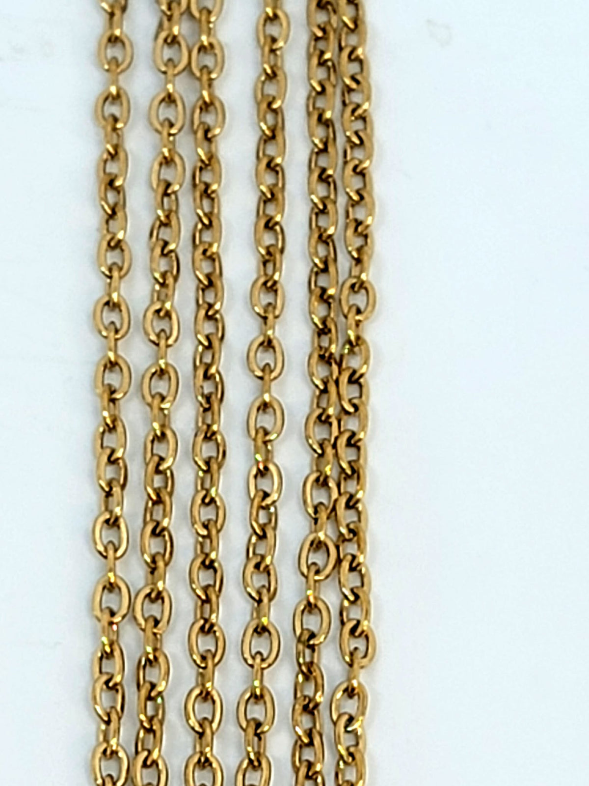 Hanging strands of 2mm gold stainless steel link chain against a white background