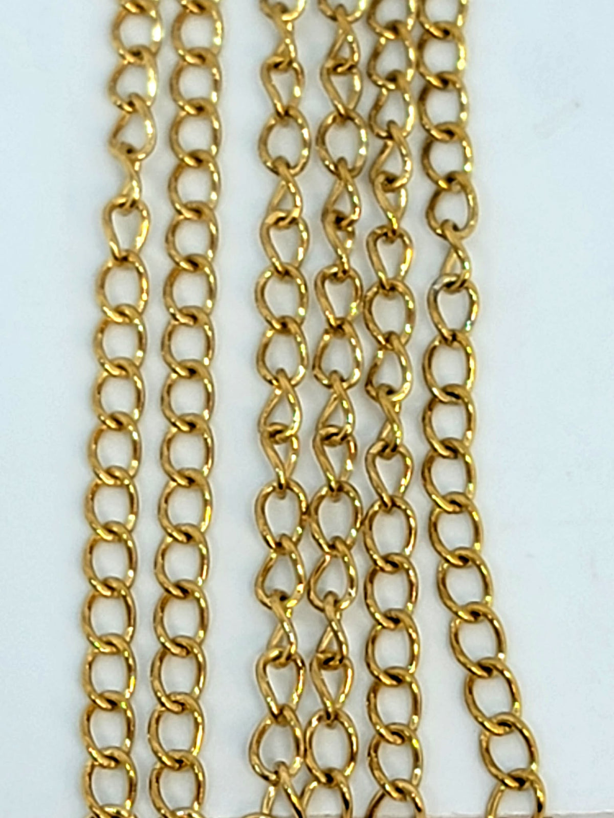 Hanging strands of 2 x 3mm gold stainless steel link chain against a white background
