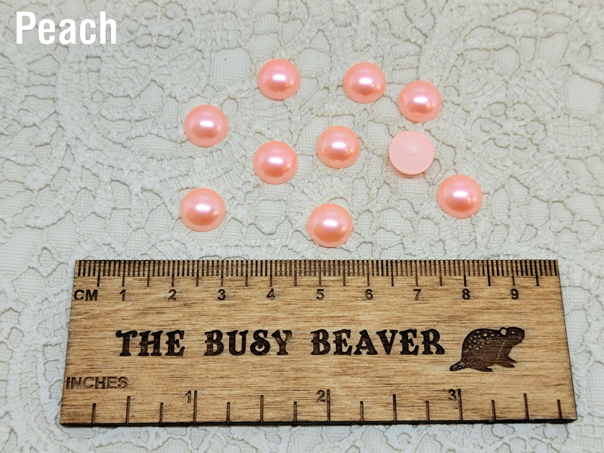 Ten 10mm peach pearl-look resin half round cabochons (cabs) beside a ruler